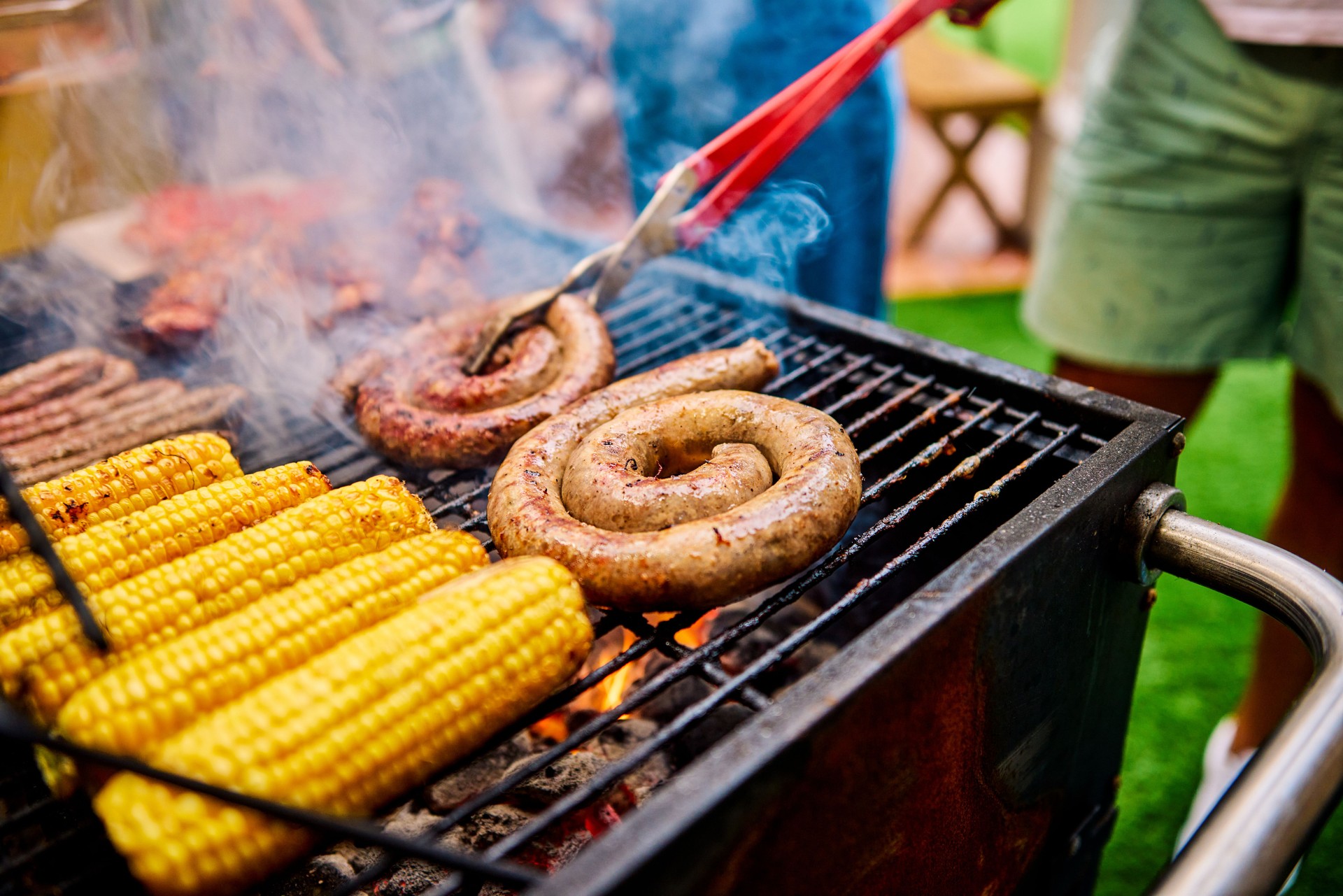 Close-up of grilling sausages and corn on an outdoor barbecue. Social gathering with food. Summer cooking and celebration concept.